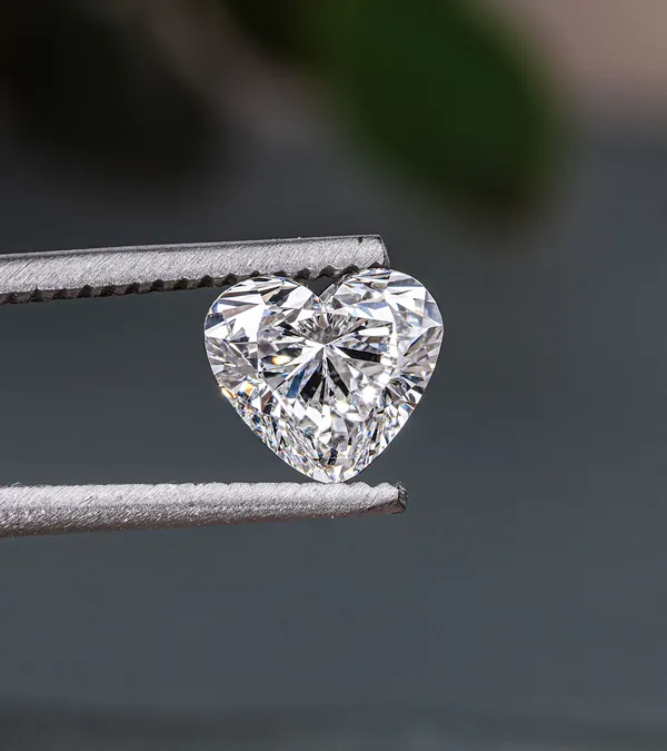 A heart-shaped natural diamond held in tweezers
